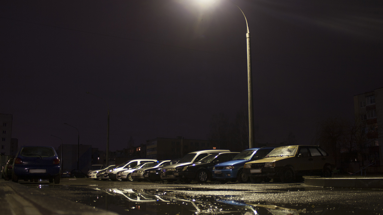 Parkende Autos auf einem beleuchteten Parkplatz vor einem Wohngebiet bei Nacht